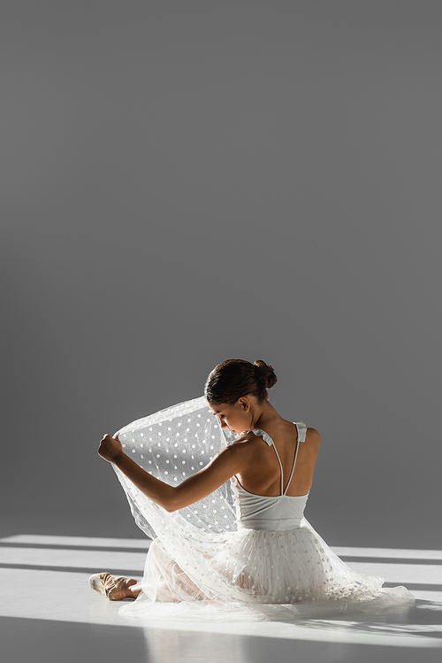 Side view of ballerina looking at skirt on grey background with sunlight