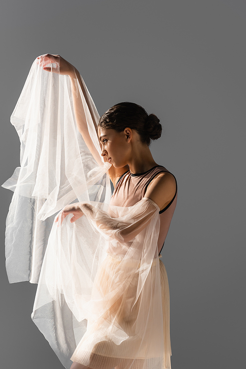 Side view of dancer looking at white cloth isolated on grey