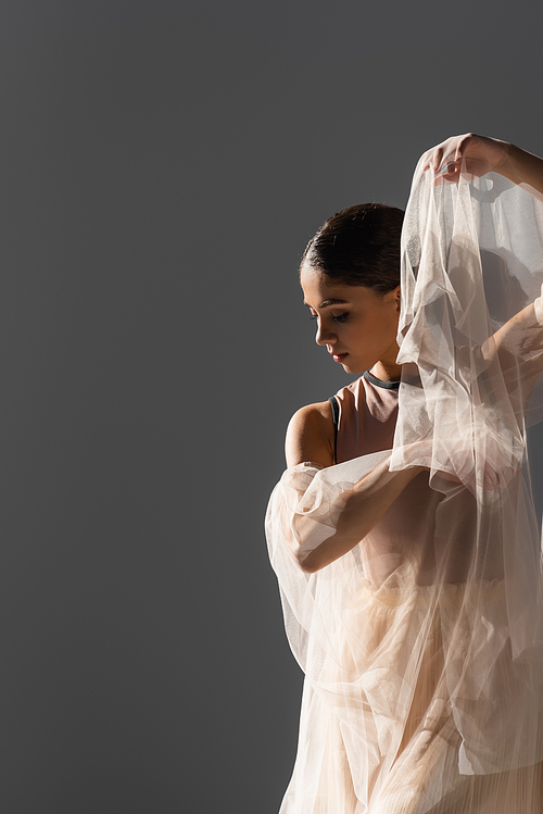 Side view of brunette dancer holding cloth in light isolated on grey