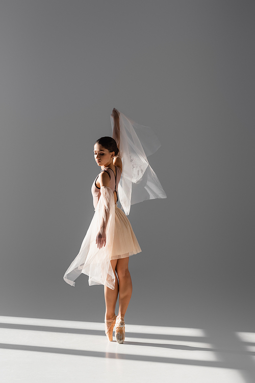 Full length of ballerina dancing with cloth on grey background with sunlight