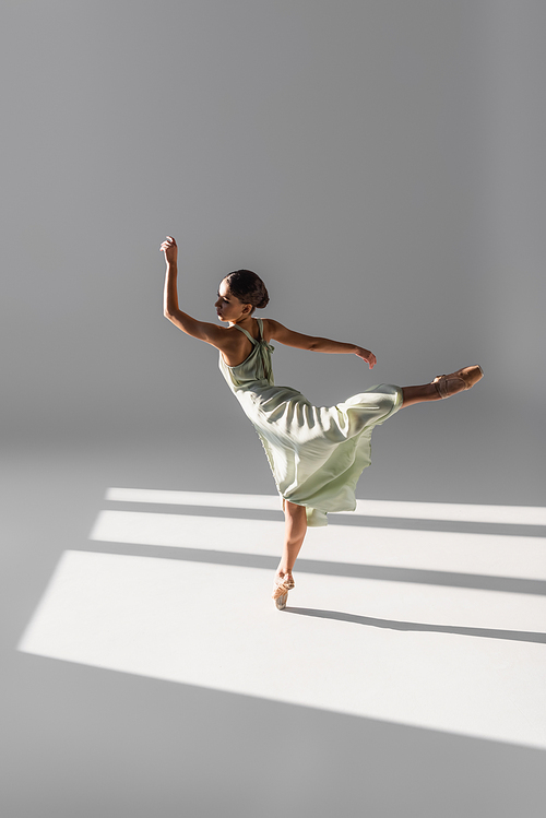 Ballerina dancing and standing on one leg on grey background with sunlight