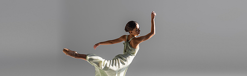 Young ballerina in pointe shoe dancing isolated on grey, banner