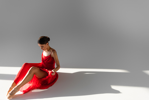 Classical dancer looking red dress on grey background with sunlight