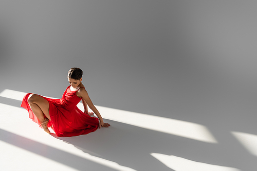 Ballerina in red dress dancing on floor on grey background with sunlight