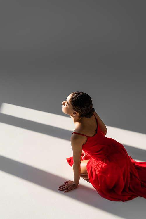 High angle view of dancer in red dress sitting on grey background with sunlight