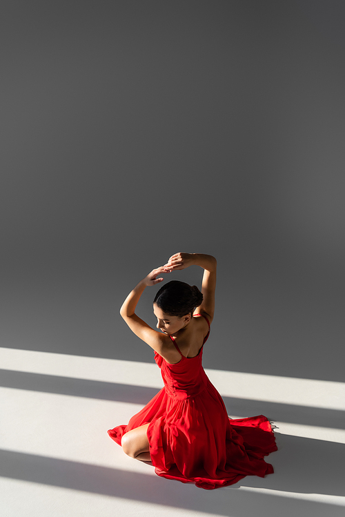 Pretty dancer in red dress posing on grey background with sunlight