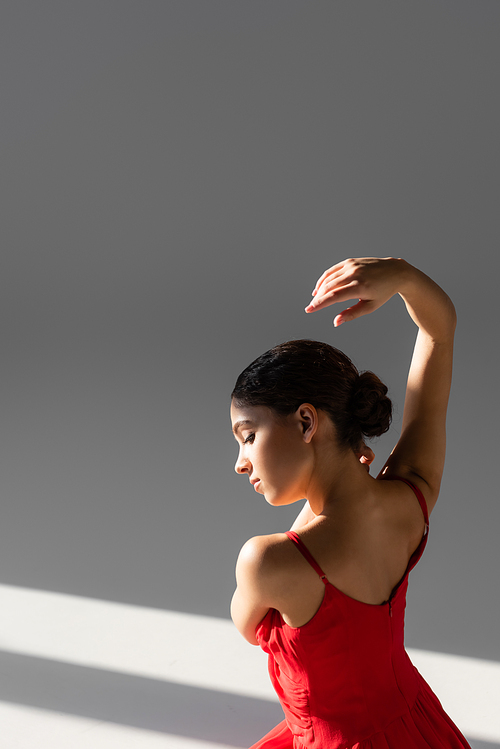 Side view of classical dancer in red dress on grey background with sunlight