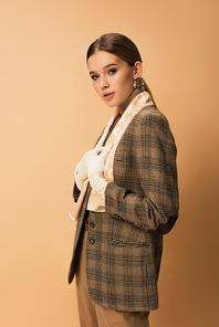 stylish woman in checkered blazer, pants and white gloves posing on beige