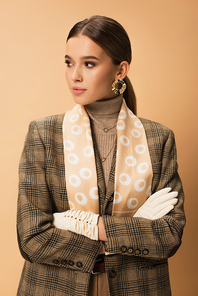 stylish woman in checkered blazer, pants and white gloves posing with crossed arms on beige