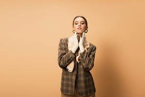 stylish woman in checkered blazer and white gloves posing on beige