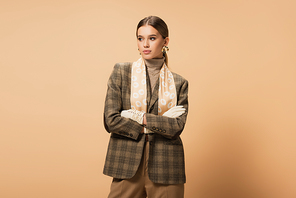 trendy woman in brown blazer and white gloves standing with crossed arms on beige
