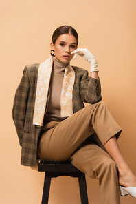 young woman in fashionable blazer and pants  while sitting on beige