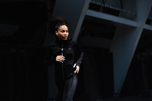 African american sportswoman in earphone running on urban street
