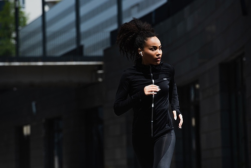 African american woman in earphone jogging on urban street