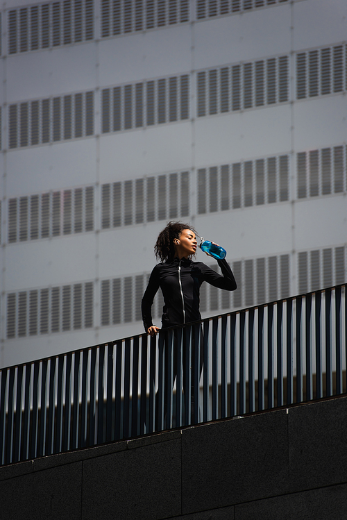 African american sportswoman drinking water on bridge on urban street