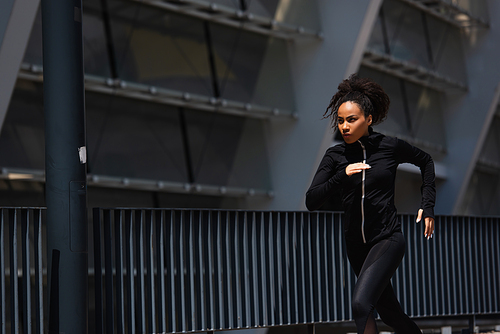 African american sportswoman in sports jacket running on urban street