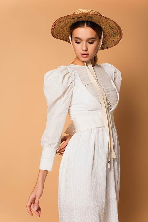 young woman in white dress and straw hat posing on beige