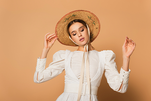 young woman in white dress adjusting straw hat on beige