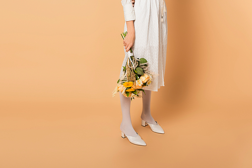 cropped view of woman in dress holding bouquet of flowers on beige