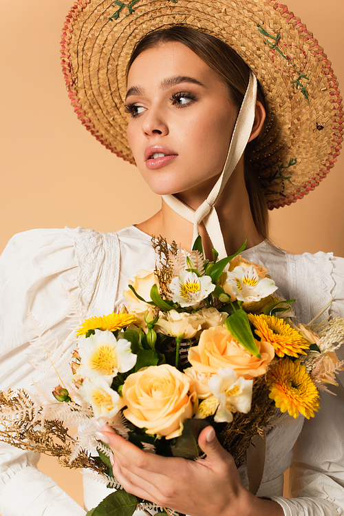 young woman in straw hat holding bouquet of flowers on beige