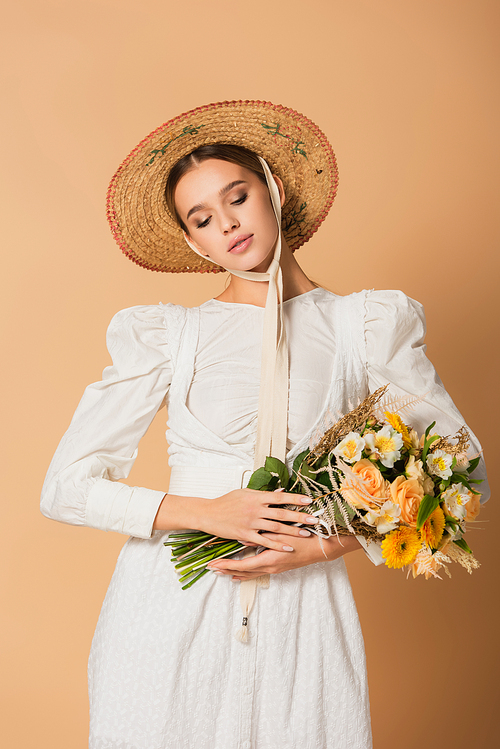 young woman in white dress and straw hat holding bouquet of flowers on beige