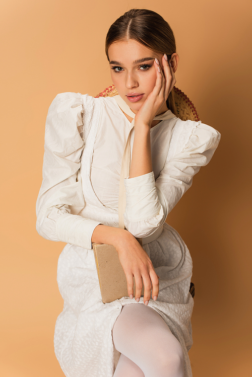 young woman in white dress posing with book on beige