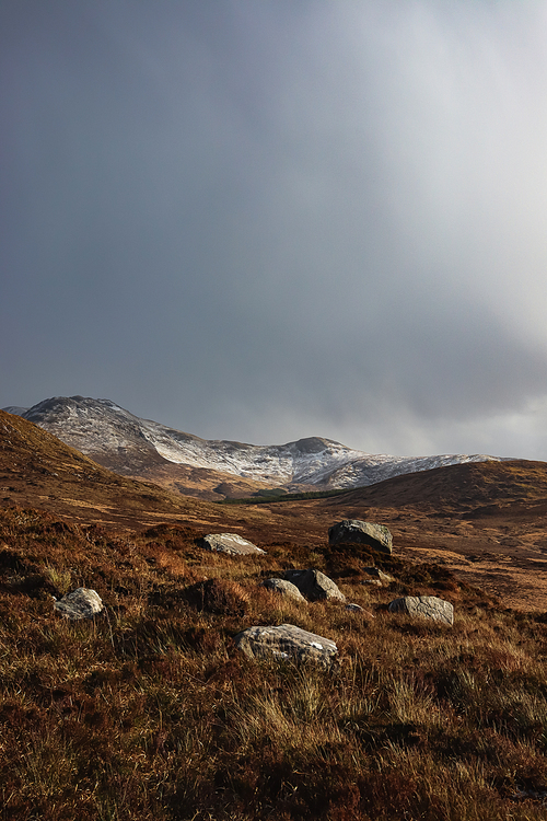 rocks on grassland near hill against cloudy sky