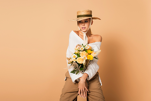 young woman in straw hat holding bouquet of flowers on beige