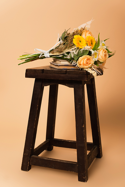 bouquet of different flowers on books and wooden chair on beige