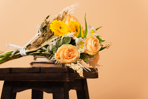 bouquet of different flowers on books and wooden chair isolated on beige