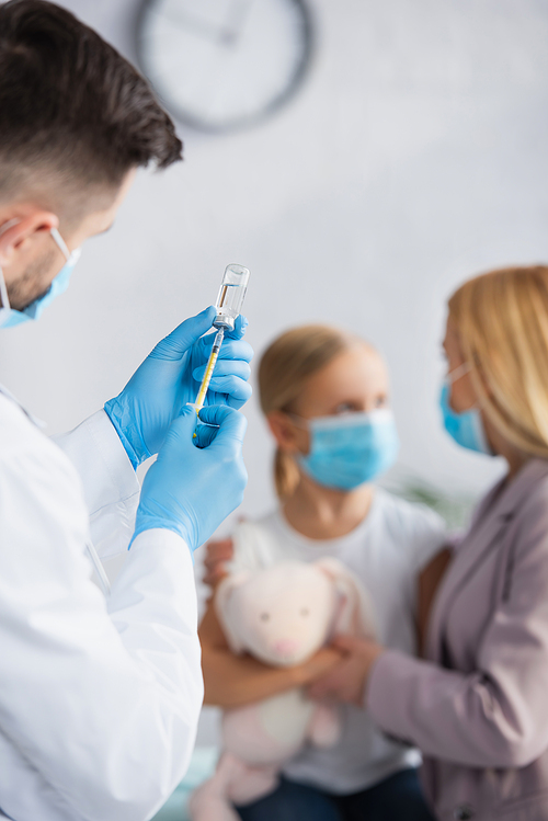 Vaccine in hands of doctor in latex gloves near family on blurred background