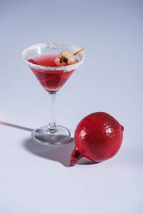 red Halloween cocktail in glass on white surface with pomegranate