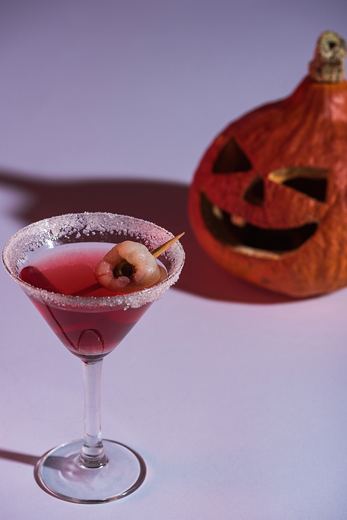 selective focus of red Halloween cocktail in glass near carved spooky pumpkin