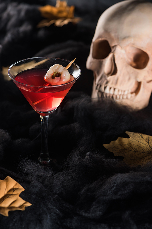 red cocktail near skull and maple yellow leaves on black background