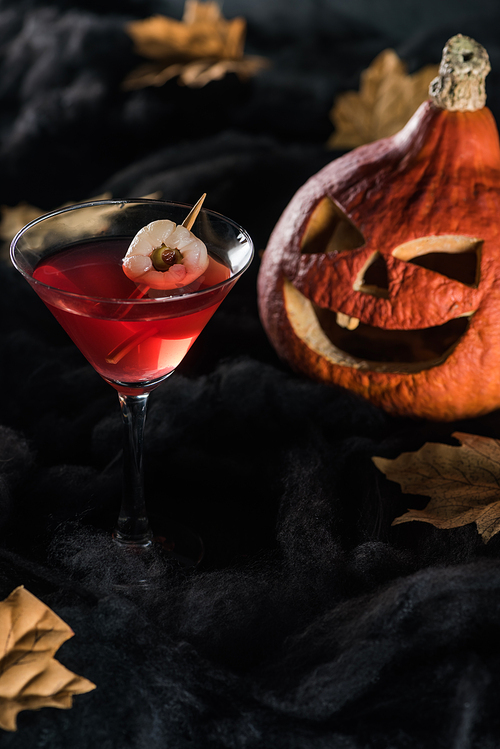 red cocktail near Halloween pumpkin and maple dry yellow leaves on black background
