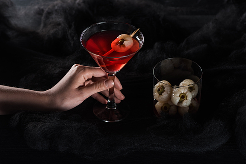 cropped view of woman holding red Halloween cocktail in black clouds