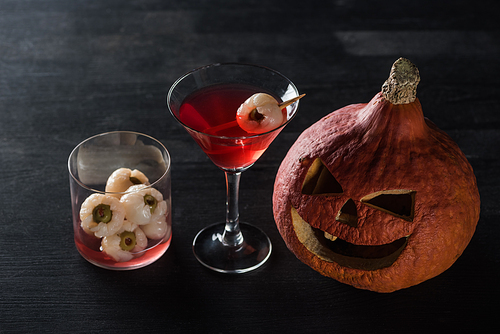 spooky carved Halloween pumpkin and red cocktail on black background