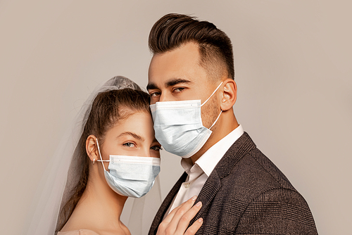 young bride and groom in medical masks  isolated on grey with lilac shade