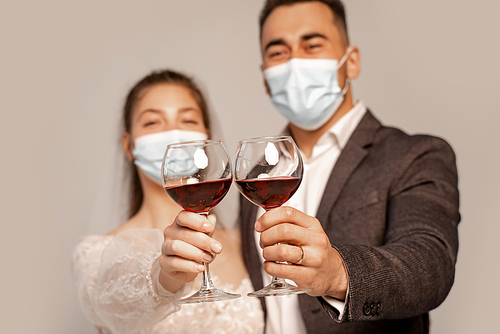 selective focus of glasses with red wine in hands of newlyweds in medical masks isolated on grey