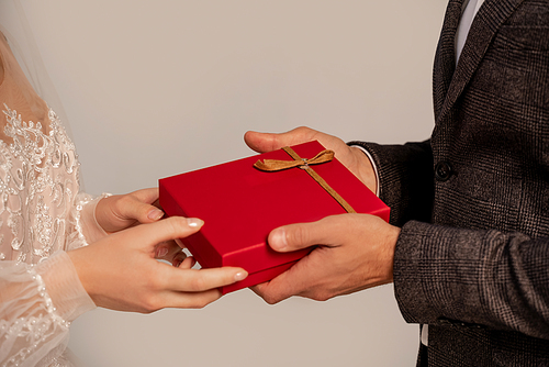 cropped view of groom presenting gift to bride isolated on grey