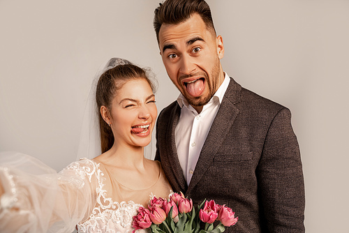 grimacing couple sticking out tongues at camera isolated on grey