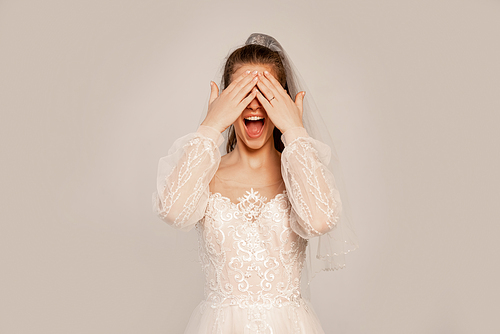 excited bride covering eyes with hands isolated on grey with lilac shade