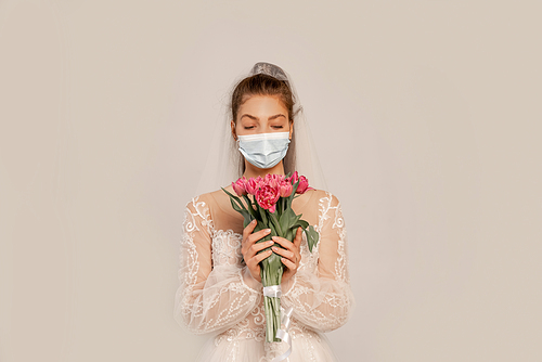 bride in medical mask holding bouquet of fresh tulips isolated on grey