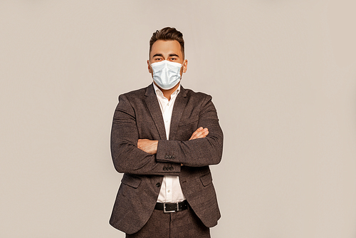 man in suit and medical mask standing with crossed arms isolated on grey