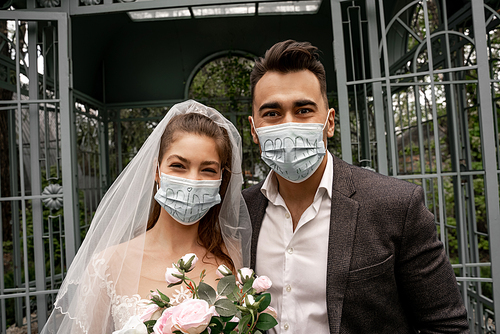 newlyweds in medical masks with bride and groom lettering  outdoors