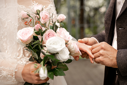 cropped view of woman with wedding bouquet near groom putting wedding ring on her finger