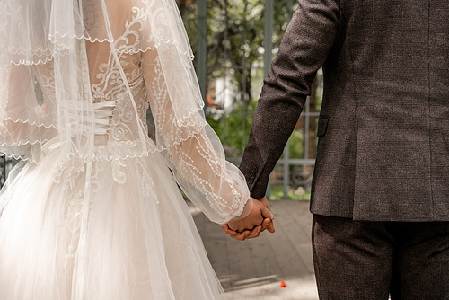 partial view of newlyweds holding hands outdoors