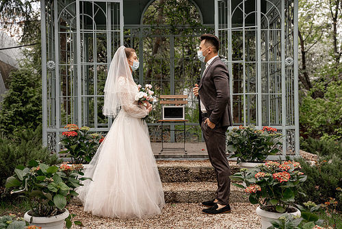 side view of bride and groom near laptop with blank screen in alcove in park