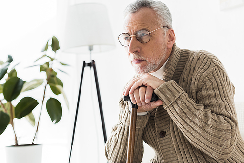 thoughtful retired man in glasses holding walking stick