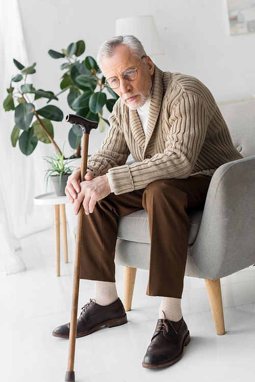 sad senior man in glasses sitting in armchair at home